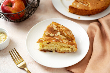 A piece of apple pie on a white plate on a light culinary background. Pie with charlotte on a platter closeup. Delicious homemade pastry on the kitchen table	