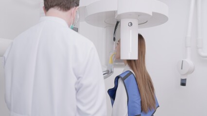 On a panoramic x-ray machine, the dentist aligns the bite of a woman. In a dental clinic, a woman...