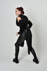 Full length portrait of pretty red haired female model wearing black futuristic scifi leather costume. Dynamic standing poses with gestural hands, facing backwards away from  on a white studio backgro © faestock