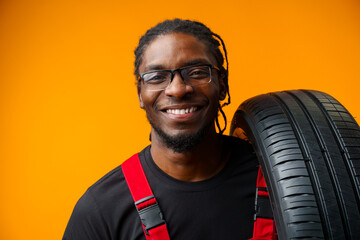 African american car service worker with car tyre against yellow background © fotofabrika