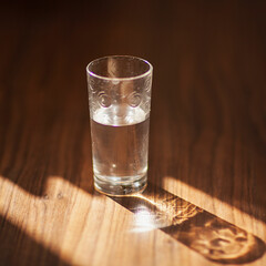 Glasses of water on a brown wooden background. Harsh light through glasses, shadows. Pure water in a glass. Simple visual concept. selective focus