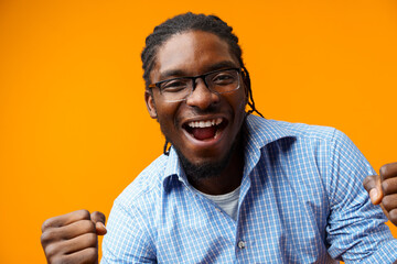 Portrait of overjoyed black man celebrating success with clenched fists against yellow background