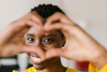 Portrait of young smiling lovely multiracial woman showing shape heart with hands and looking...