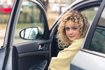 Pretty curly haired Caucasian woman sits in the car smiling car purchase concept copy space portrait . High quality photo
