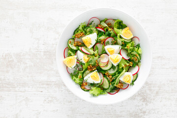 Easter fresh vegetable salad with boiled egg, radish and cucumber, dressing with dijon mustard and lemon on white wooden table. Top view