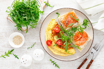 Omelette or omelet, fresh arugula and tomato salad and toasts with butter and salted salmon. Breakfast. Top view