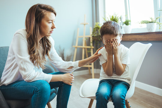 Children need help. Upset little boy crying in psychologist's office unable to control emotions, sharing problems and traumas, professional psychotherapist comforting kid, side view