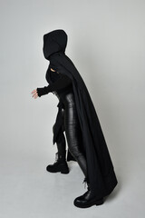 Full length portrait of pretty red haired female model wearing black futuristic scifi leather costume with black flowing cloaked cape. Dynamic standing poses with gestural hands, facing backwards away