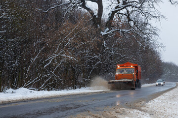 A large car with a plow clears the road from snow. Orange cargo special equipment is struggling...