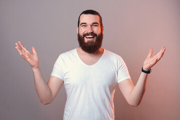 Photo of youn man with beard smiling and showing welcome gesture, nice to meet you.