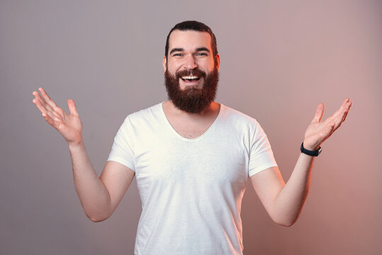 Photo of youn man with beard smiling and showing welcome gesture, nice to meet you.