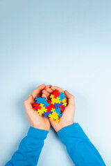 Child hand holding colorful puzzle heart on light blue background. World autism awareness day...