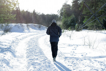 Man runs in the winter along a wide forest road lit by bright sunlight.