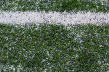 The football field with artificial green grass is covered with a light layer of snow. Early spring....