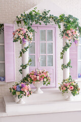 facade of a white and lilac building with a porch decorated with flowers. Photo zone in the photo studio