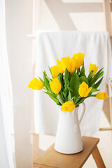 bouquet of yellow tulips in a white ceramic vase on the background of the window. Sunny photo