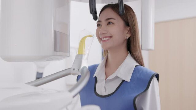 On a panoramic x-ray machine, the dentist aligns the bite of a woman. In a dental clinic, a woman dressed in a lead apron stands still as a panoramic X-ray machine circles her head.