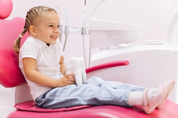 Little girl smiling on a visit to the dentist holding a tooth model at the dental clinic