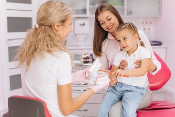 Little girl with mom visiting female dentist at dental clinic