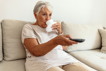 Senior woman enjoying at her living room, watching TV. Senior woman enjoying at her living room, watching TV and drinking coffee.