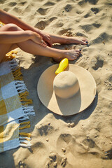 Top view Woman leg sitting on the sandy beach, near hat and sunscreen