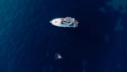 Aerial view of slim woman swimming on the swim ring in the blue sea near yacht in Adriatic sea. Summer seascape with girl, beautiful waves, blue water in sunny day. Top view from drone