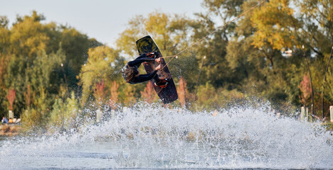 Wakeboarder making tricks while wakeboarding on lake. Young man surfer having fun wakesurfing in...