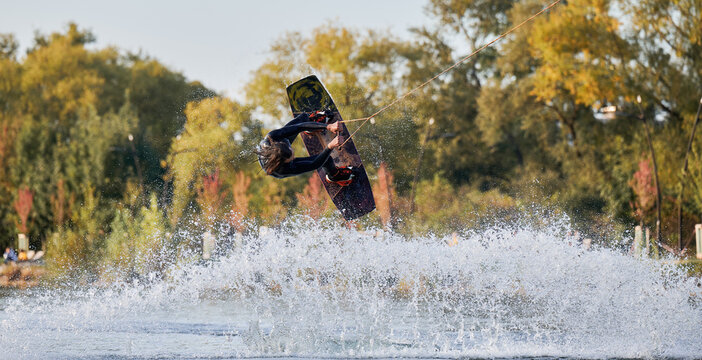 Wakeboarder making tricks while wakeboarding on lake. Young man surfer having fun wakesurfing in the cable park. Water sport, outdoor activity concept. - Powered by Adobe