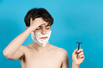 Worried teenager boy looking at razor isolated on blue background