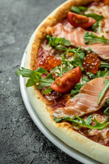 Delicious hot pizza with salmon, red caviar, tomatoes and aragula ready to eat. vertical image. top view. place for text
