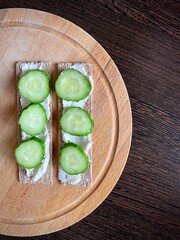 large vertical photo. Crips with curd cheese and cucumber slices on a brown wooden board. eco. bio. organic products. diet food.