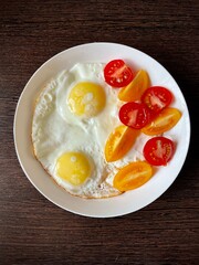 large vertical photo. fried eggs with slices of red and yellow tomatoes on a white plate. eco. bio. organic products. diet food.