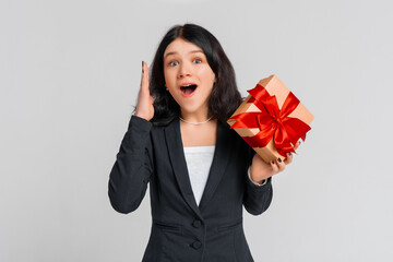 Happy excited brunette teenager girl in black blazer with gift box, standing over white background....