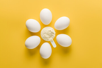 scoop with egg white and several eggs on a yellow background.