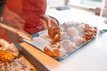 Fresh homemade Cinnamon rolls or Cinnamon buns are on a baking sheet board, and there is an unrecognizable person wearing an apron in the background.