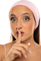 Portrait of young excited woman holding finger on lips on a white background