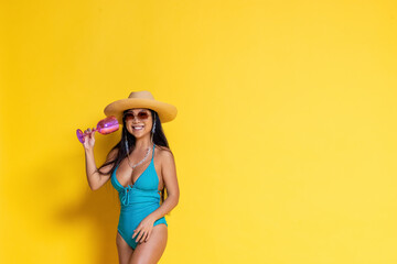 Fototapeta na wymiar Beautiful asian girl in swimsuit and a hat with wineglass in her hand on a yellow background