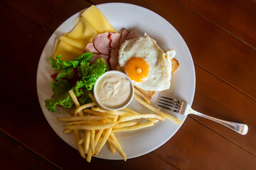 American breakfast with scrambled eggs, toast, french fries, salad, cheese and ham on a white plate in the daylight