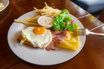 American breakfast with scrambled eggs, toast, french fries, salad, cheese and ham on a white plate in the daylight