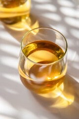 glass of white wine or apple juice, cider on white background with harsh shadows, natural light, bright golden drink