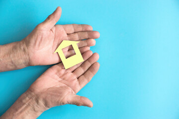 In the hands of an elderly man, a paper-cut house on a blue background. The concept of savings, mortgages and buying an apartment. Right copyspace.