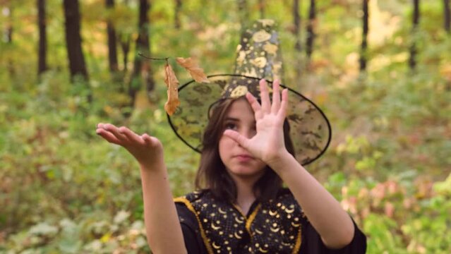 Close up photo of a young girl dressed in Halloween clothes making magician signs to hold leaves in air.