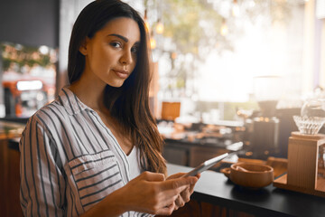 Technology makes it easy to run things. Cropped portrait of an attractive young woman working on a digital tablet while standing in her coffee shop.
