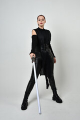 Full length portrait of pretty red haired female model wearing black futuristic scifi leather...