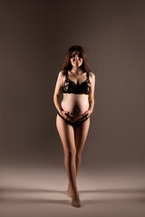 Fototapeta premium Pregnant woman in lingerie hugs her belly with her hands