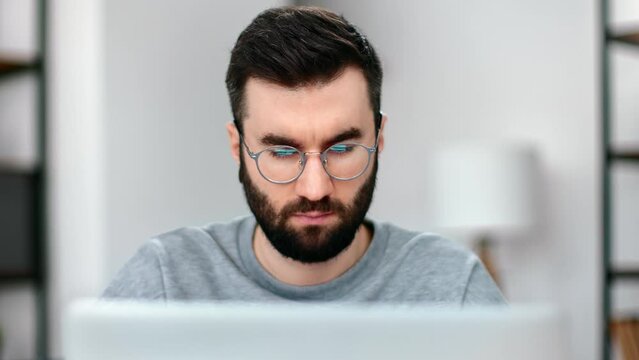 Closeup confident man in eyeglasses working laptop browsing internet at modern home office
