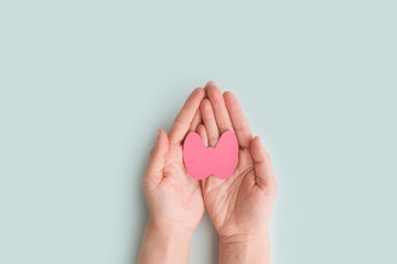 World Thyroid Day. Women's hands hold a paper form of the thyroid gland on a blue background....