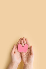 Fototapeta na wymiar World Thyroid Day. Women's hands hold a paper form of the thyroid gland on beige background. Problems with thyroid. Polycystic disease. World cancer day. copy space