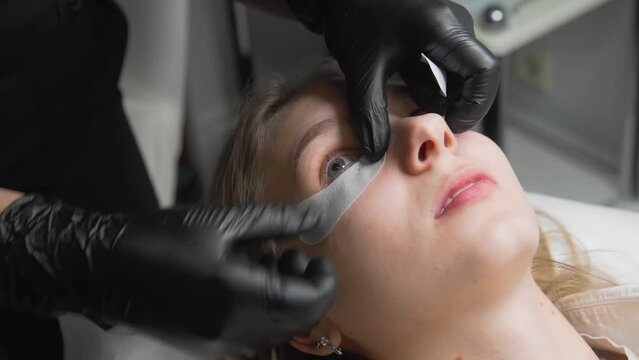 Close-up of a female face of a young girl and a professional cosmetologist performing modern spa-cosmetic procedures for laminating eyelashes. Spa treatments.