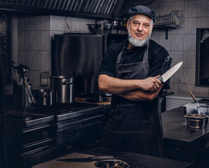 Cool old man chef holding knife in modern kitchen